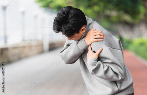 Asian man is suffering from shoulder pain with hand covering on it. 