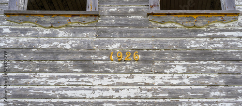Fotografie Image of an old, dilapidated building with pealing white paint and the date 1926 in yellowish-orange numbering