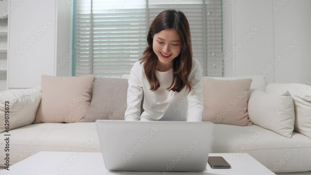 Happy asian woman using laptop computer device technology working sitting on couch at home. Smiling asian young woman searching internet website or online studying from home. Lifestyle concept Happy asian woman using laptop computer device technology working sitting on couch at home. Smiling asian young woman searching internet website or online studying from home. Lifestyle concept