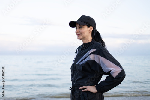Close-up portrait of a beautiful brunette woman wearing fashion sports suit and cap looking at sunset on the beach © Petr