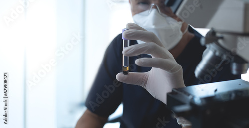 Doctor or technician holding a blood sample test tube with microscope in hospital laboratory room. Medical research, blood test for diagnosis, medical lab background