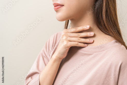Sickness in inflaming asian young woman, girl use hand check self touch at sore throat, pain thyroid gland on neck or disease reflux, acid of suffer people on wall background. Medical and healthcare.