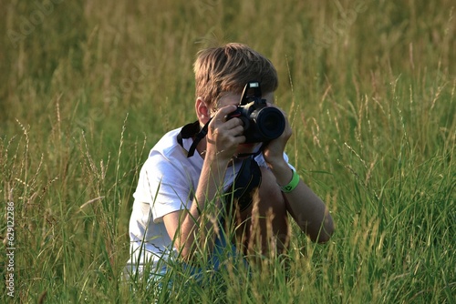 Obraz na plátně boy sitting in the grass with a reflex camera