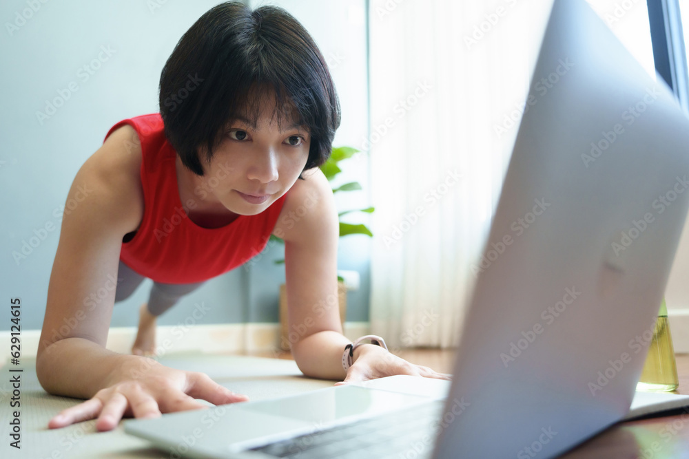 Portrait of Sporty Asian Chinese woman doing yoga plank and watching online class on laptop. Wellness, Healthcare Concept Portrait of Sporty Asian Chinese woman doing yoga plank and watching online class on laptop. Wellness, Healthcare Concept