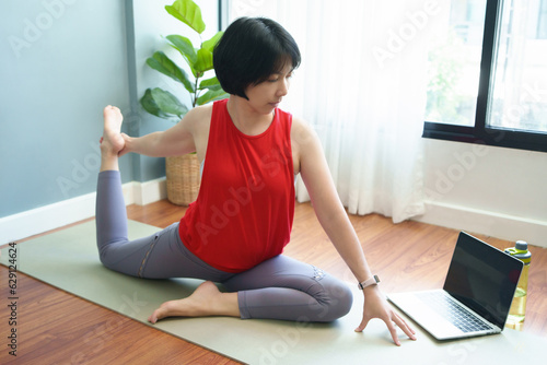 Healthy Asian female practice yoga exercise in online class with laptop. Wellness, Healthcare Concept