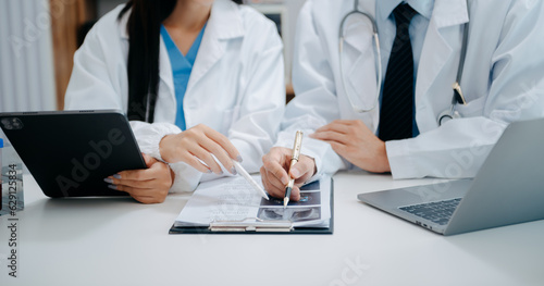 Medical team having a meeting with doctors in white lab coats and surgical scrubs seated at a table discussing a patients working online using computers in the medical industry.