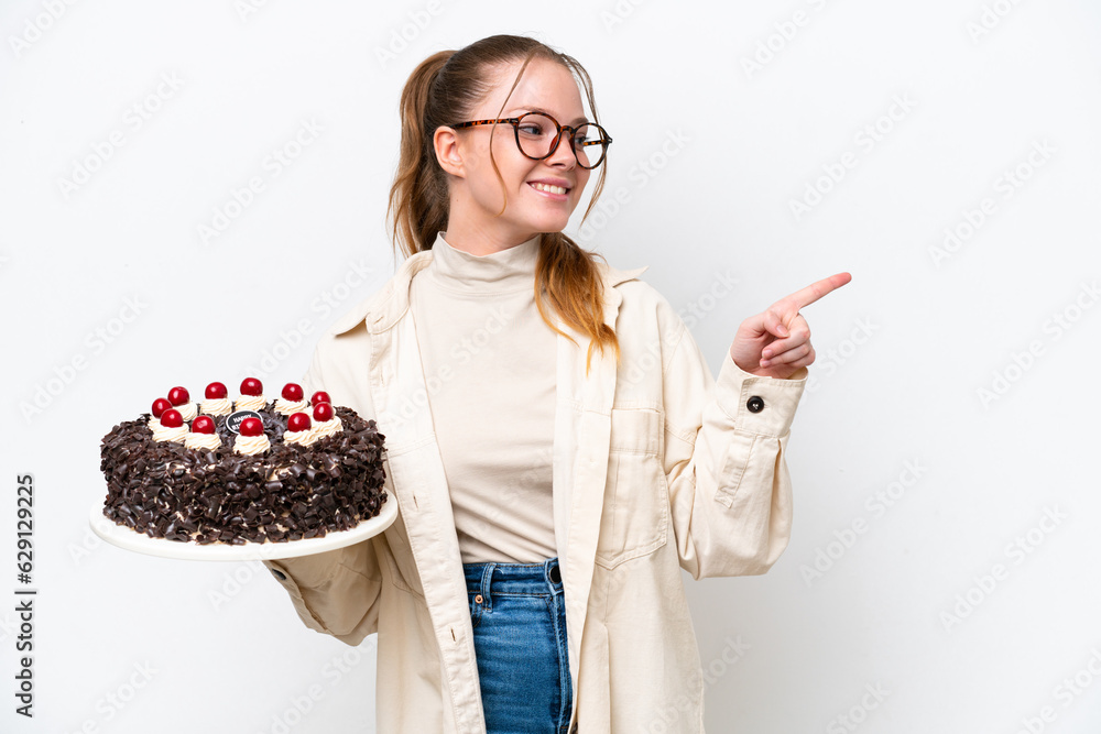 Young caucasian woman holding a Birthday cake isolated on white background pointing finger to the side and presenting a product Young caucasian woman holding a Birthday cake isolated on white background pointing finger to the side and presenting a product