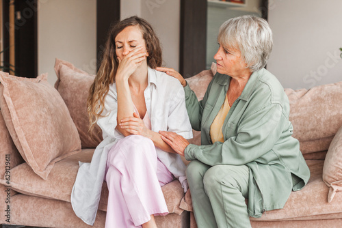 Worried aged mother embracing comforting sad grown up daughter with broken heart family sit on sofa