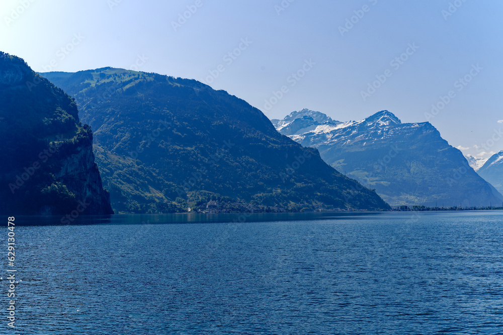 Scenic mountain panorama with Lake Lucerne in the foreground and Swiss village Flüelen in the background on a sunny spring day. Photo taken May 22nd, 2023, Lake Lucerne, Switzerland. Scenic mountain panorama with Lake Lucerne in the foreground and Swiss village Flüelen in the background on a sunny spring day. Photo taken May 22nd, 2023, Lake Lucerne, Switzerland.