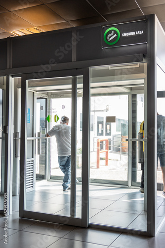 Smoking room or cabin at departure hall of airport with unrecognized people smoking within