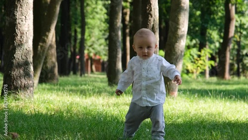 Baby takes first steps. Baby boy running in the park. Happy baby takes first steps in nature. Toddler walks on grass in park. Baby learns to walk. Happy family kid concept 4k