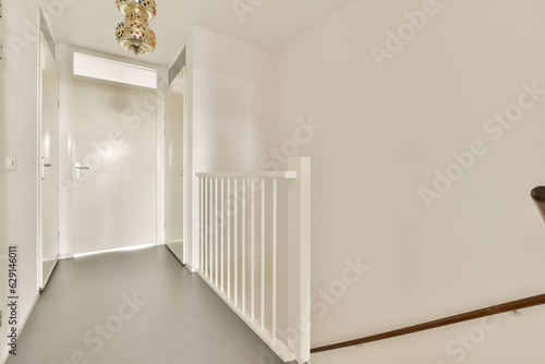 a hallway with white walls and wooden stairs leading up to the second floor there is a chandel on the right handrail photo