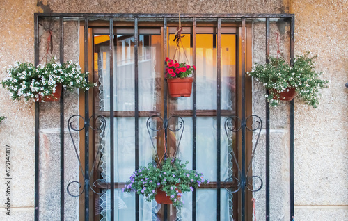 Ventana con cristal y rejas donde cuelgan unas macetas con plantas en flor. Casa de arquitectura moderna, pero tradicional en Hoyos del Espino, Ávila, España.  photo