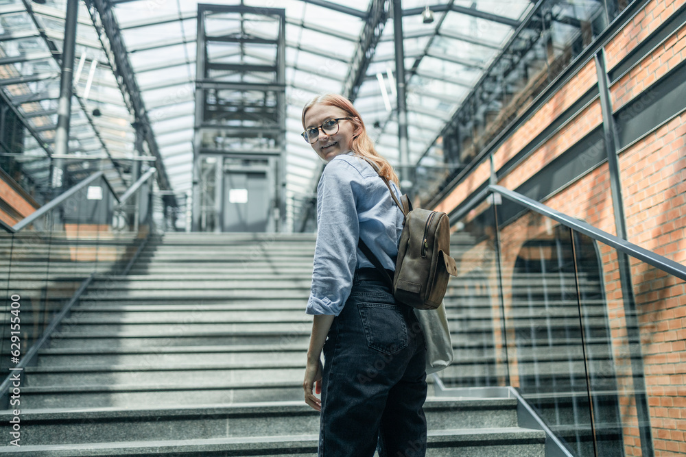 Happy businesswoman or student with backpack climbing the stairs in modern loft style hall. Road to success concept. High quality photo Happy businesswoman or student with backpack climbing the stairs in modern loft style hall. Road to success concept. High quality photo
