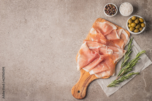 Thin slices of Italian prosciutto with green olives, spices and rosemary on wooden cutting broad. Raw dried meat. photo