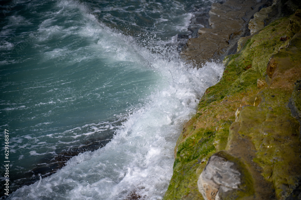 The sea wave hitting the stone mossy shore