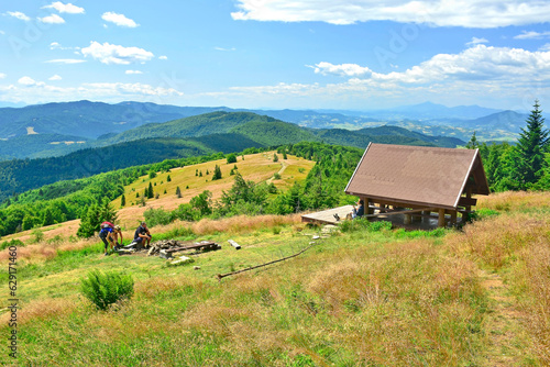 Fototapeta Naklejka Na Ścianę i Meble -  Group of tourists relax, socialize and picnic on weekends at mountains meadow and wooden hut in summer sunny day, Mogielica, Island Beskids (Beskid Wyspowy), Poland