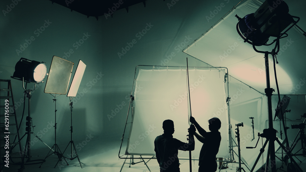 Silhouette of video production behind the scenes or B roll or making of TV commercial movie that film crew team lightman and cameraman working together with director in big studio with pro equipments - obrazy, fototapety, plakaty 