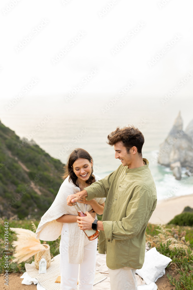 Romantic loving couple opening a champagne bottle, having romantic date on nature with beautiful view, vertical shot Romantic loving couple opening a champagne bottle, having romantic date on nature with beautiful view, vertical shot