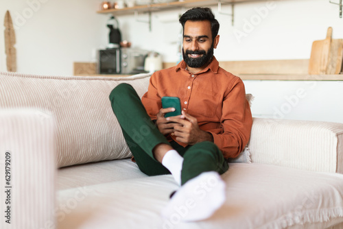 Middle Eastern Guy texting on smartphone and websurfing at home © Prostock-studio