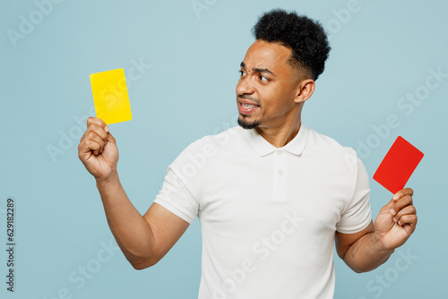 Fotografie Young man fan wear basic t-shirt cheer up support football sport team hold choose between yellow red card propose player retire from field watch tv live stream isolated on plain blue color background