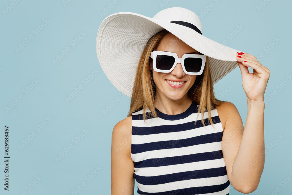 Young beautiful woman she wears striped tank shirt casual clothes sunglasses hat look camera with toothy smile isolated on plain pastel light blue cyan background studio portrait. Lifestyle concept. Young beautiful woman she wears striped tank shirt casual clothes sunglasses hat look camera with toothy smile isolated on plain pastel light blue cyan background studio portrait. Lifestyle concept.