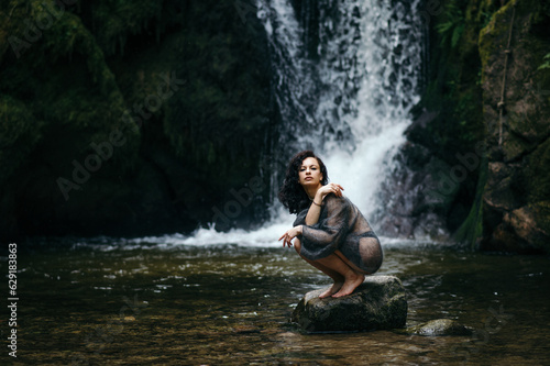Beautiful young woman sitting on rock near mountain river in forest. High quality photo