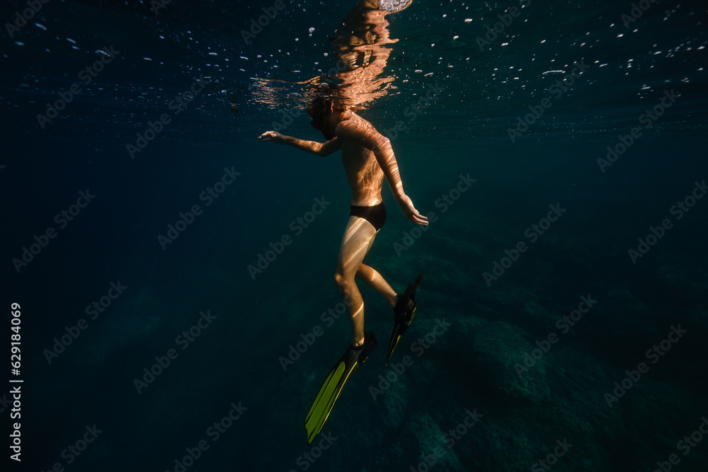 Anonymous male tourist diving undersea in sunlight