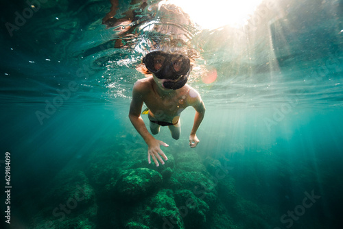 Young guy in snorkeling goggles swimming underwater of sea