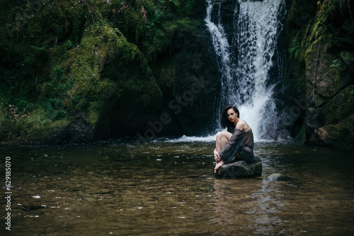Beautiful young woman sitting on rock near mountain river in forest. High quality photo