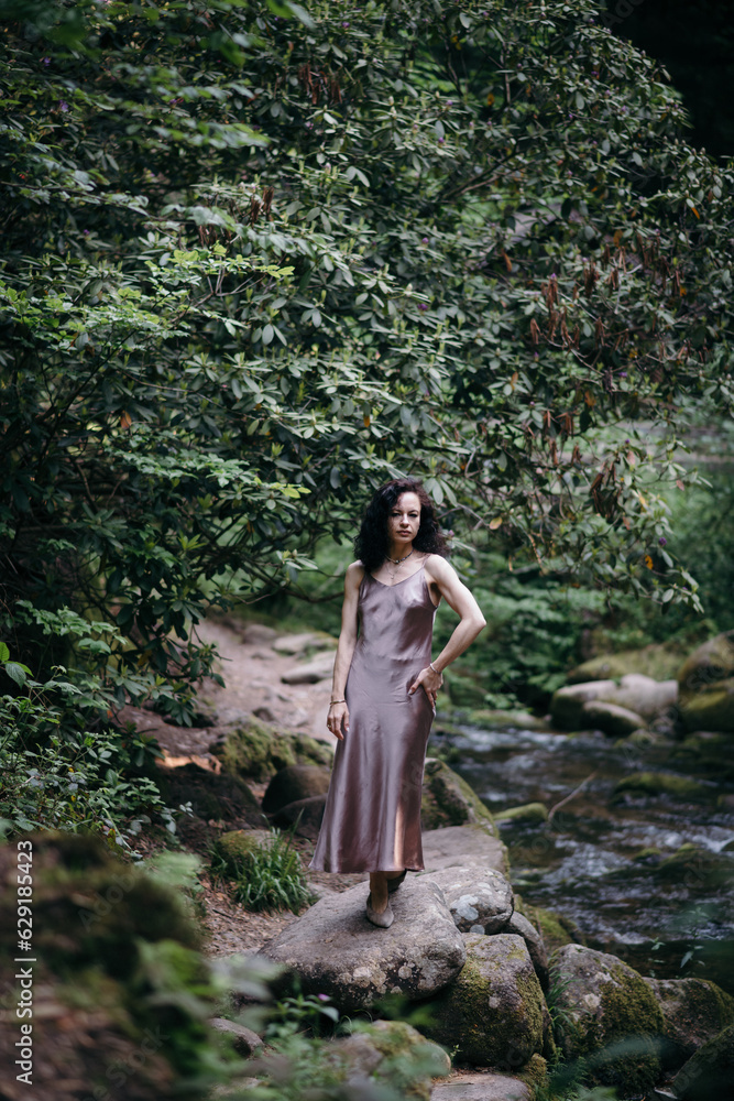 Fototapeta premium Beautiful young woman sitting on rock near mountain river in forest. High quality photo