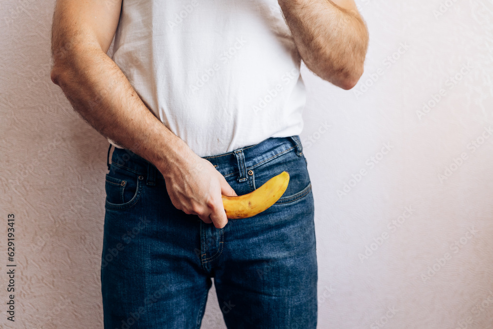 The guy is holding a banana in his jeans. Men's health prostate prevention - obrazy, fototapety, plakaty 