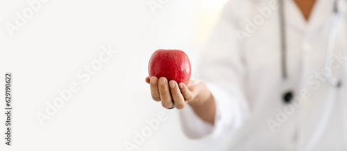 Mature caucasian lady doctor nutritionist in white coat show apple in office interior, panorama photo