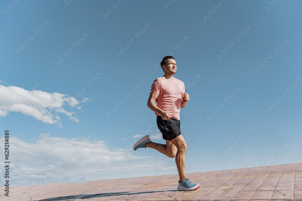 A young man jogging in a T-shirt and shorts, running alone on a treadmill in the city. Active lifestyle and motivation. A young man jogging in a T-shirt and shorts, running alone on a treadmill in the city. Active lifestyle and motivation.