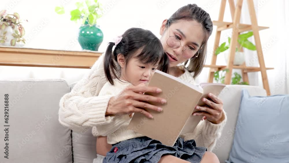 Asian beautiful pregnant mother reads a book with her eldest daughter in the living room during their leisure time, mom teaching baby to read, Telling stories to little child. family happiness concept Asian beautiful pregnant mother reads a book with her eldest daughter in the living room during their leisure time, mom teaching baby to read, Telling stories to little child. family happiness concept
