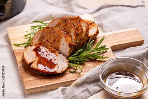 Baked Pork Loin sliced on a wooden board with Tangy Mustard and Herb sauce and rosemary sprigs