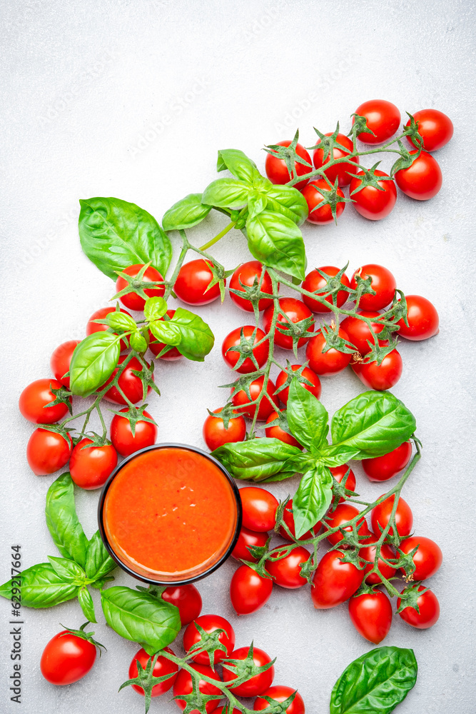 Freshly squeezed tomato juice in a glass and red cherry tomatoes on branches with green basil on gray table, food background, top view Freshly squeezed tomato juice in a glass and red cherry tomatoes on branches with green basil on gray table, food background, top view