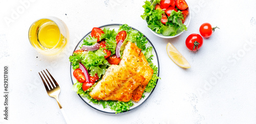 Fried white fish with salad from lettuce, cherry tomatoes and red onion with sesame seeds, white table background, top view