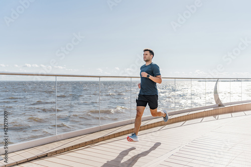 Motivation a male trainer does sports beautifully running. A happy athlete is a person. Using a smartwatch, a runner guy in fitness clothes looks at the time. © muse studio