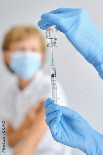 Crop nurse filling syringe with vaccine against patient in hospital