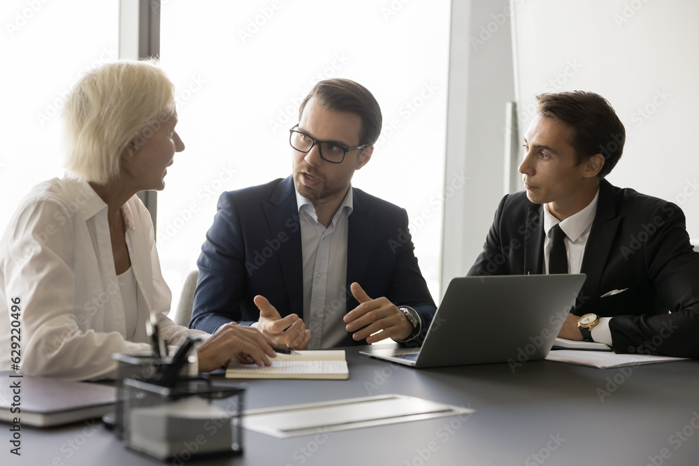 Business project leader discussing marketing strategy with employees, planning tasks, teamwork, talking to colleagues, partners, sitting at meeting table with laptop Business project leader discussing marketing strategy with employees, planning tasks, teamwork, talking to colleagues, partners, sitting at meeting table with laptop