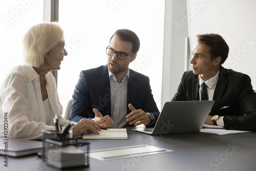 Business project leader discussing marketing strategy with employees, planning tasks, teamwork, talking to colleagues, partners, sitting at meeting table with laptop