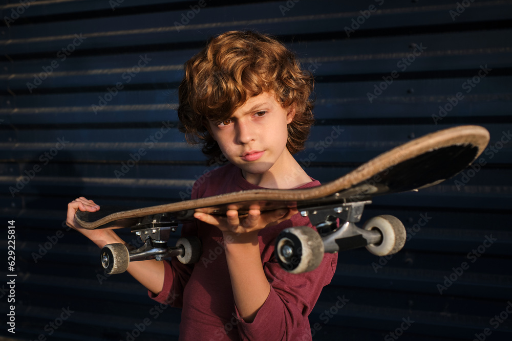 Boy examining skateboard against blue wall