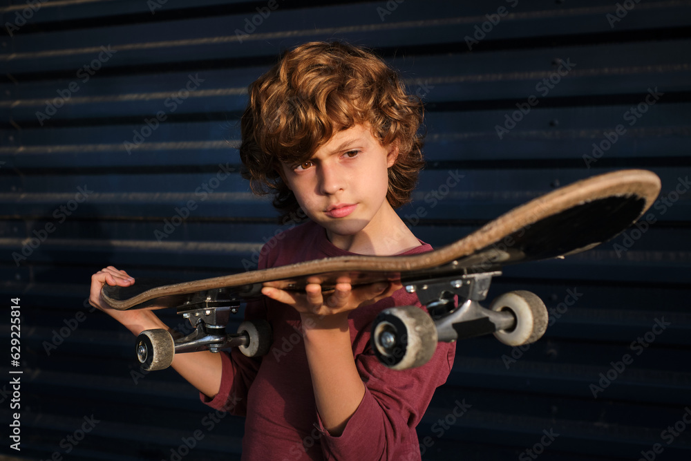 Fototapeta premium Boy examining skateboard against blue wall