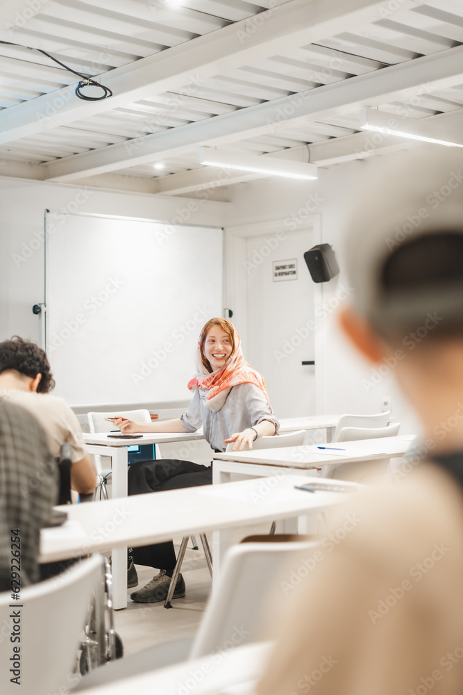 Obraz premium Happy, overjoyed, muslim female employee listening to her coworker joking at the middle of the meeting. Businesswoman wearing hijab smiling