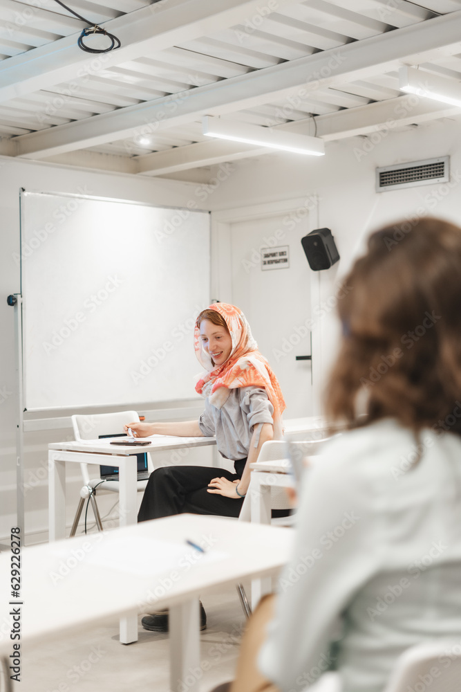 Obraz premium Female redhead employee wearing hijab looking at something during presentation and smiling