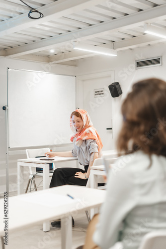 Female redhead employee wearing hijab looking at something during presentation and smiling