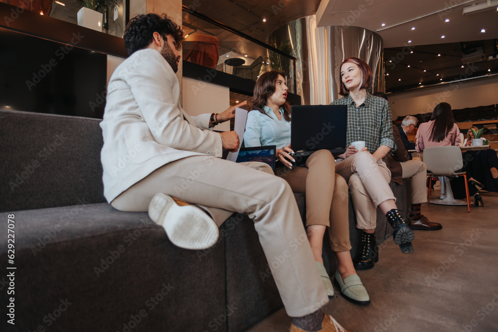Young employees working together at the office sitting on a grey sofa. Male business person explaining possible scenario to his female partners