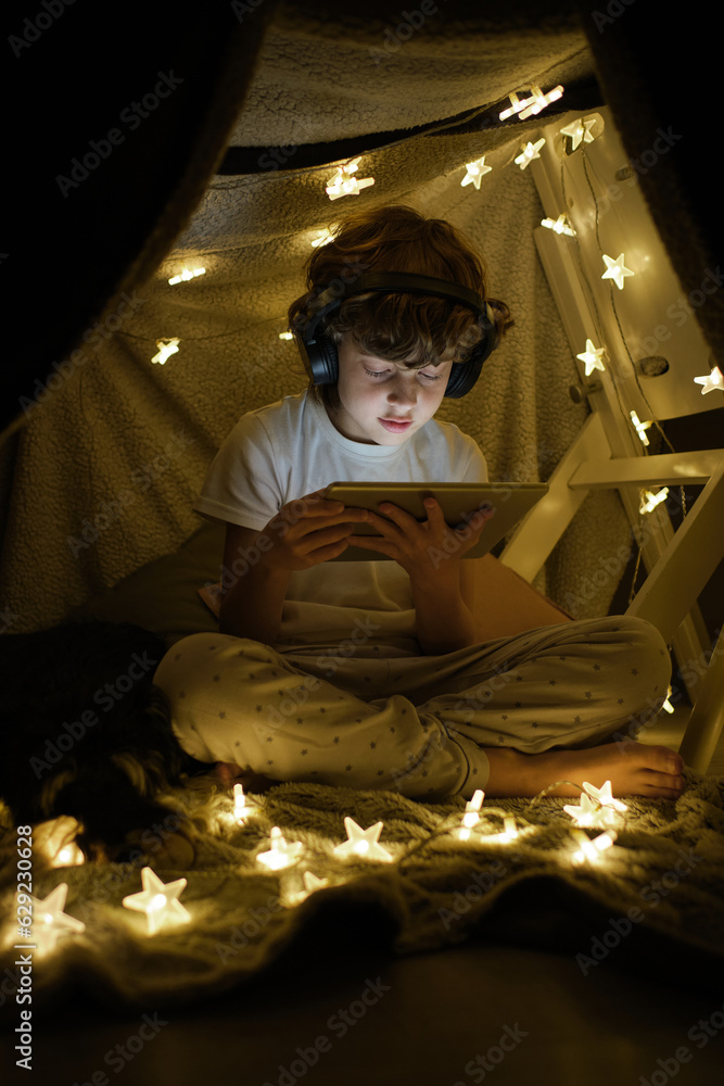 Focused boy browsing tablet on blanket fort