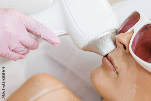 The cosmetologist does the procedure for laser hair removal of unwanted hair of the face to a young girl in a beauty salon. Dermatology, photorejuvenation. Cosmetic clinic.